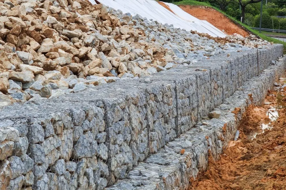 Muro de arrimo em gabião de pedra contendo encosta de terra com manta geotêxtil Muro de arrimo em gabião de pedra contendo encosta de terra com manta geotêxtil